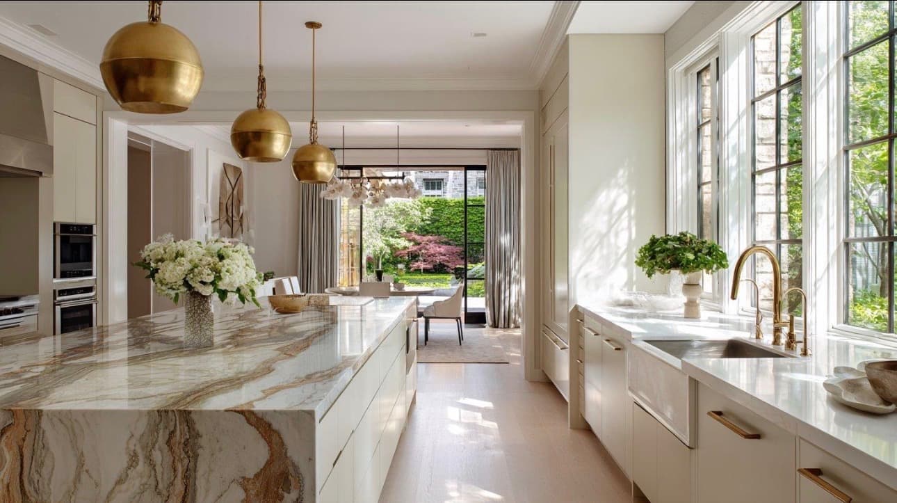 Clean, sunlit kitchen with a marble island and brass pendant lights